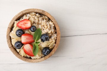 Tasty oatmeal with strawberries, blueberries and almond petals in bowl on white wooden table, top...