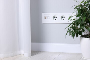 Electric power sockets on light grey wall indoors, space for text