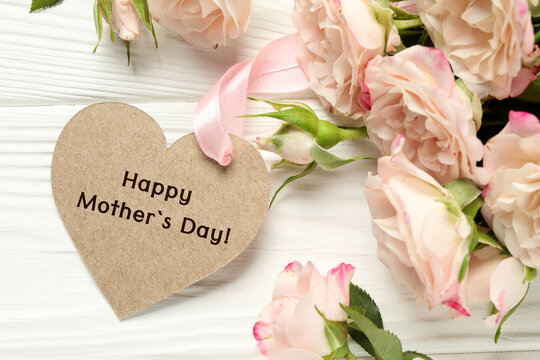 Happy Mother's Day. Heart shaped greeting label and beautiful flowers on white wooden table