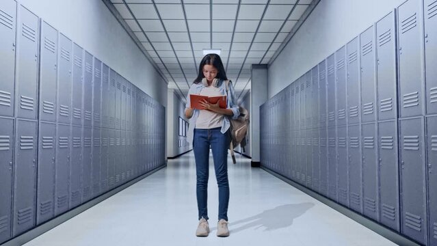 Full Body Of Asian Teen Girl Student With A Backpack Taking Note On Notebook And Thinking Then Raising Her Index Finger While Standing in Corridor