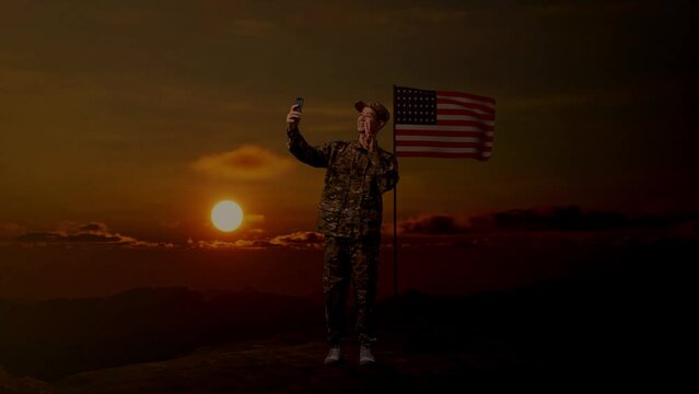 Full Body Of Asian Man Soldier Using Smartphone Taking Picture While Standing With Flag Of The United States, Sunset Time