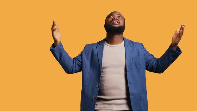 Cheerful pious african american man looking up to sky, waiting for sign from his god. Happy spiritual man doing worship hand gesturing, hoping for miracle, isolated over studio background, camera B