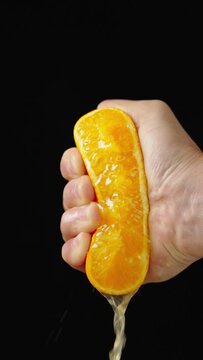 Woman's hand squeezing half a juicy orange on black background in slow motion.
