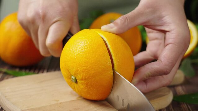 woman cutting a ripe orange in half on a cutting board