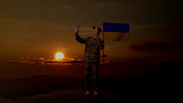 Full Body Of Asian Man Soldier Using Smartphone Taking Picture While Standing With Flag of Ukraine, Sunset Time