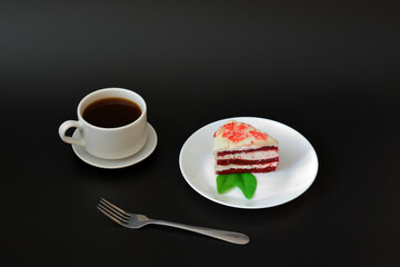 A plate with a piece of cake Red velvet decorated with mint leaves and a cup of hot black coffee on a saucer with a fork on a black background.