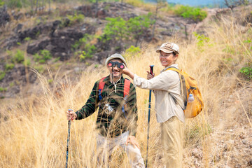 active senior couple in hiking clothes,standing on the hill,a wife left hand pass the binoculars to...