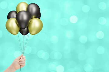 Female hand holds bunch of golden and black balloons on blurred green background. Empty space for text - 784889505