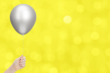 Kids hand holds silver balloon on blurred yellow background. Empty space for text - 784889506