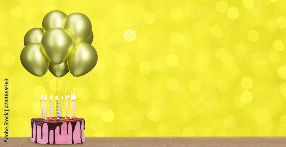 Poster chocolate birthday cake with many candles and bunch of golden balloons on blurred yellow background.