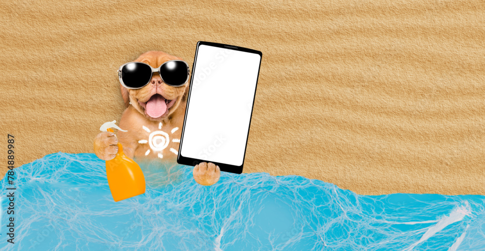 Poster Funny Mastiff puppy at beach applying suntan lotion or sun block and showing big smartphone with white blank screen in it paw. Empty space for text