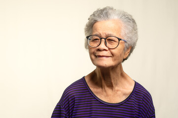 Portrait of an elderly Asian woman looking at the camera with a smile while standing on a gray...