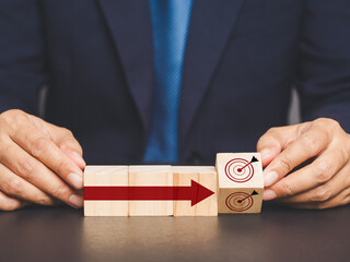 Close-up of hands arranging wooden blocks with arrows and target symbols, business strategy concept.