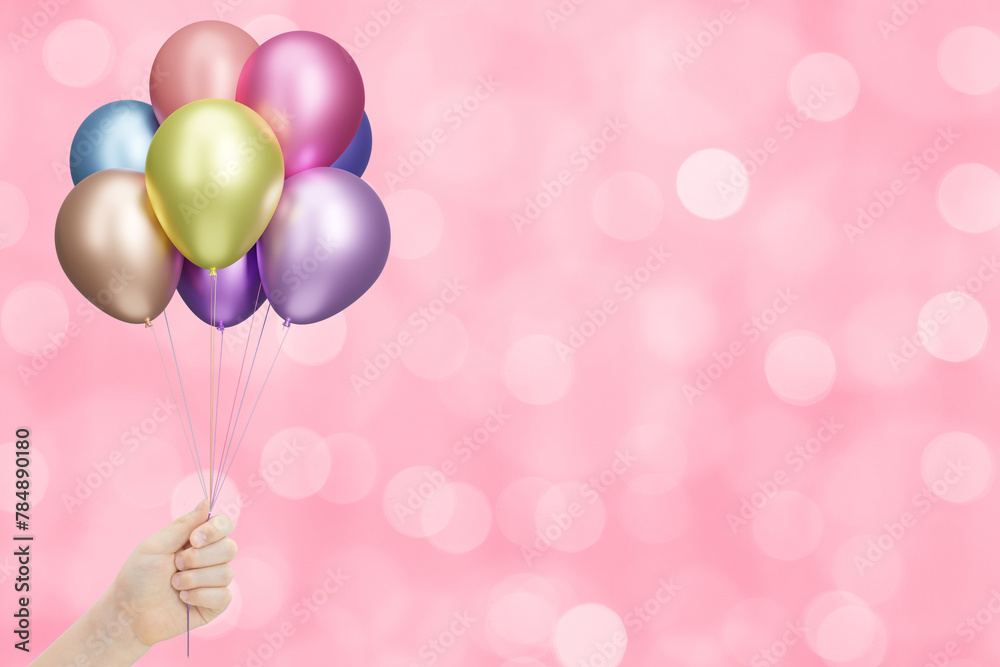Poster childrens hand holds bunch of colorful shiny balloons on blurred pink background. empty space for te