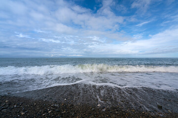 An incoming wave on the Black Sea and a pebble beach on the Sochi coast on a sunny summer day with clouds, Sochi, Krasnodar Territory, Russia