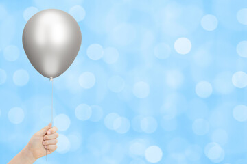 Kids hand holds silver balloon on blurred blue background. Empty space for text