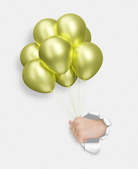 Childrens hand holding yellow or golden shiny balloons through the hole in white paper