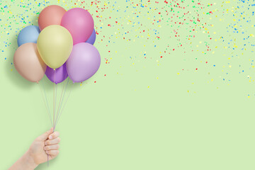 Female hand holds bunch of colorful balloons on mint background with confetti. Empty space for text