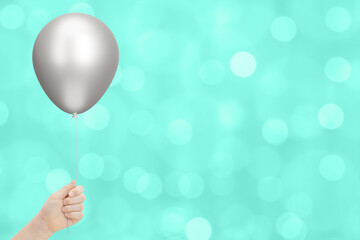 Kids hand holds silver balloon on blurred aquamarine background. Empty space for text