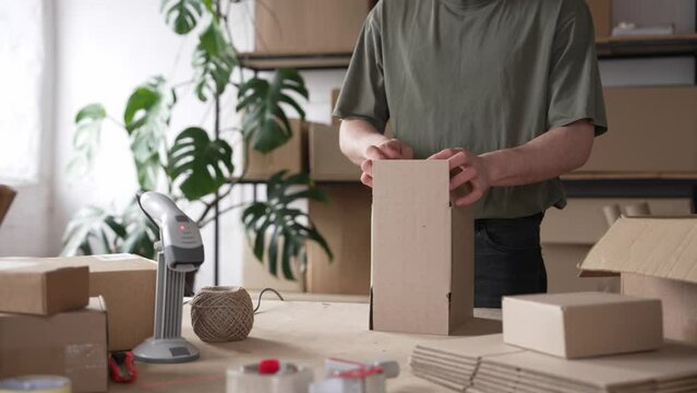 A young businessman, a retailer, packs goods in corrugated cardboard boxes. Ecommerce business