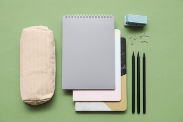 Beige pencil case with different school stationery and notebooks on green background © Pixel-Shot