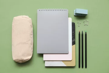Fotobehang Beige pencil case with different school stationery and notebooks on green background © Pixel-Shot