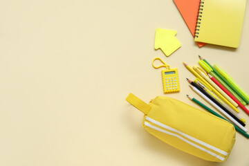 Yellow pencil case with different school stationery and notebooks on beige background