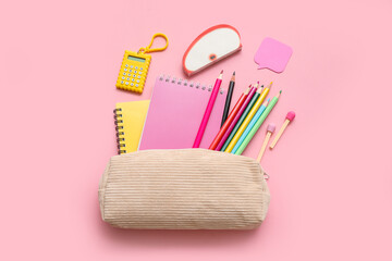 Beige pencil case with different school stationery and notebooks on pink background
