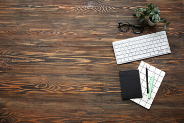 Computer keyboard, eyeglasses and stationery on wooden background