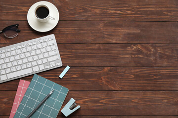 Computer keyboard, cup of coffee and stationery on wooden background