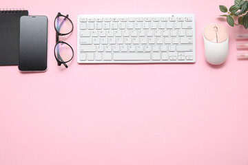 Computer keyboard with mouse, phone and eyeglasses on pink background