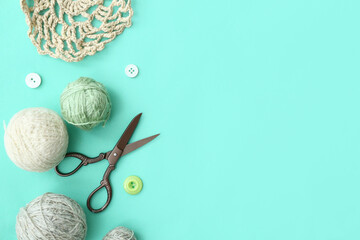 Yarn balls, buttons and scissors on turquoise background