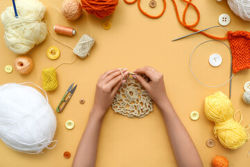 Woman hands with knitting needles, yarn balls and buttons on beige background