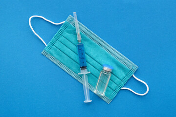 Medical syringe with medicine, mask and ampoule on blue background