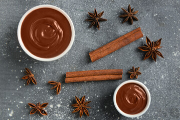 Bowls of tasty melted chocolate with cinnamon sticks and star anise on grey grunge background