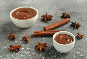 Obraz na płótnie Canvas Bowls of tasty melted chocolate with cinnamon sticks and star anise on grey grunge background