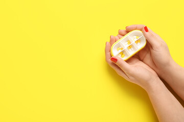 Female hands and container with pills on yellow background