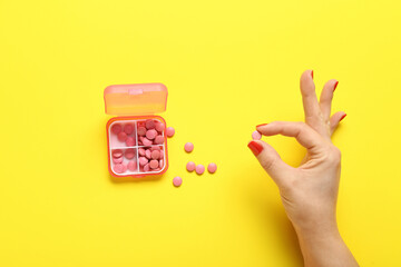 Female hand and container with pills on yellow background