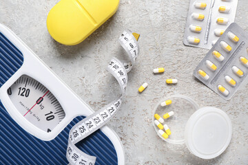 Containers with weight loss pills, scales and measuring tape on grey grunge background