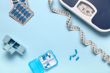 Frame made of container with weight loss pills, scales and measuring tape on blue background