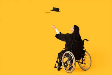Beautiful female graduate student in wheelchair with graduation cap on yellow background