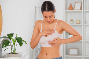 Beautiful young woman checking her breast in bathroom. Cancer awareness concept