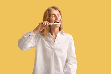 Young woman brushing her teeth on yellow background