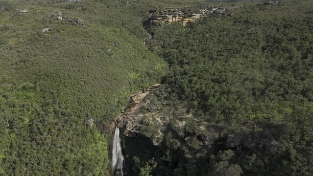 Drone descends on Véu das Noivas waterfall on sunny afternoon in Parque das Andorinhas