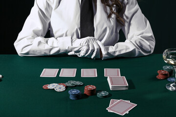 Woman sitting at poker table with playing cards and chips on black background, closeup