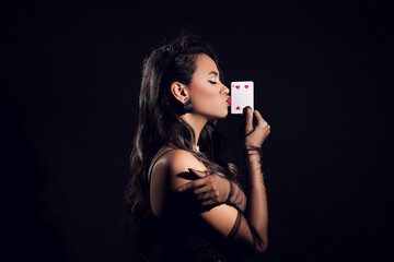 Beautiful young African-American woman kissing playing card on black background