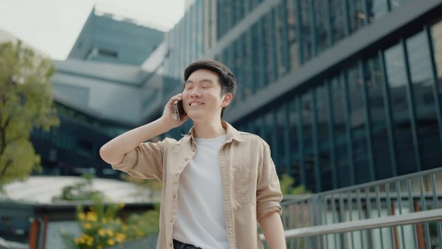 Handsome Asian student using smartphone. A young man standing outdoor happy smiling with holding mobile phone