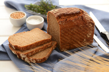 Sliced loaf of bread with salt and wheat grains on white wooden background
