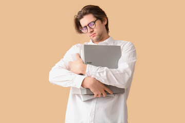 Weary young businessman with laptop on beige background - obrazy, fototapety, plakaty