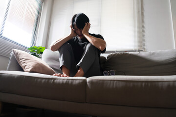 Man with mental health problem sitting on couch and use hands to covering ears from noise anything